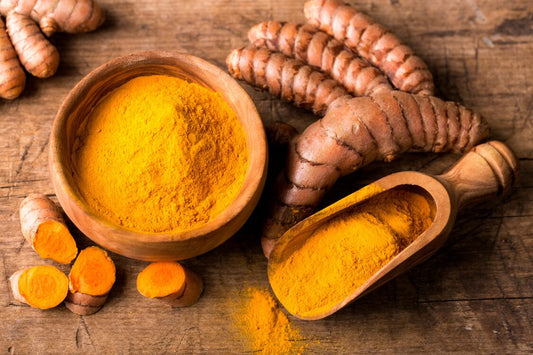 wooden bowl of ground turmeric curcumin, bright orange powder, with wooden spoon and turmeric roots on a wooden countertop