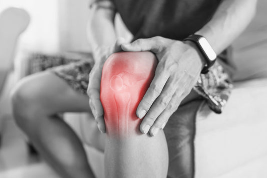 Grey black and white image, with the knee highlighted in red to show the joint pain of man sitting down in a pair of shorts