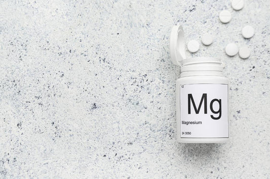 Tub of magnesium tablets with white tablets coming out of it on a grey background