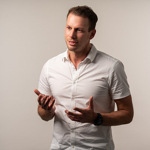 Doctor Dominik Pretz talking with his hands, white shirt, and a natural grey coloured background