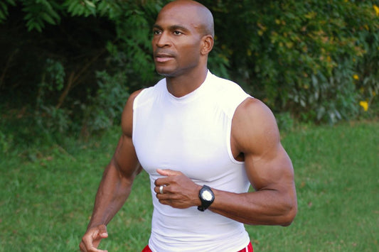 Muscular black man wearing a white vest top, jogging through a green landscape trees and grass