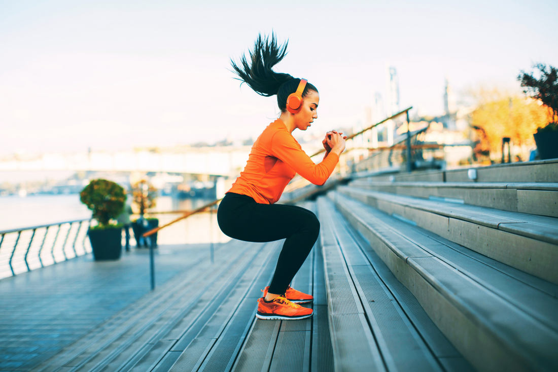 A woman with an orange fitness outfit, jumping steps outdoors for an exercise regime