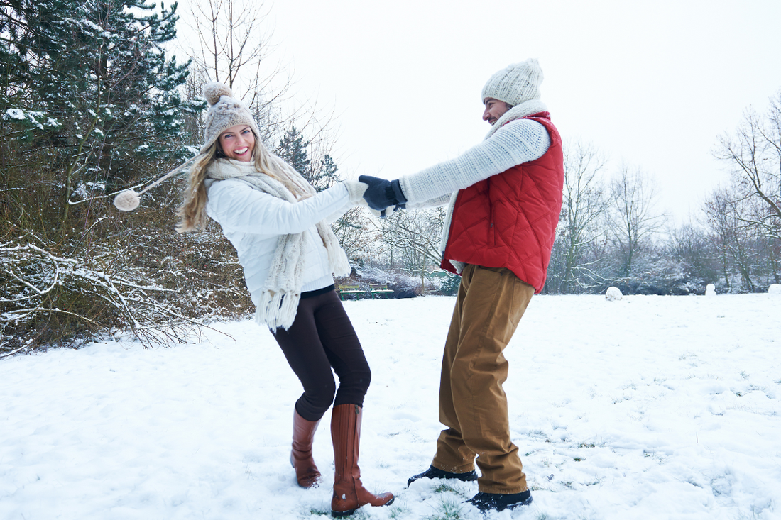 two people outdoors in the snow, forest, woodlands, laughing, holding hands, winter clothes, happy, beating winter blues, white sky, january blues, winter