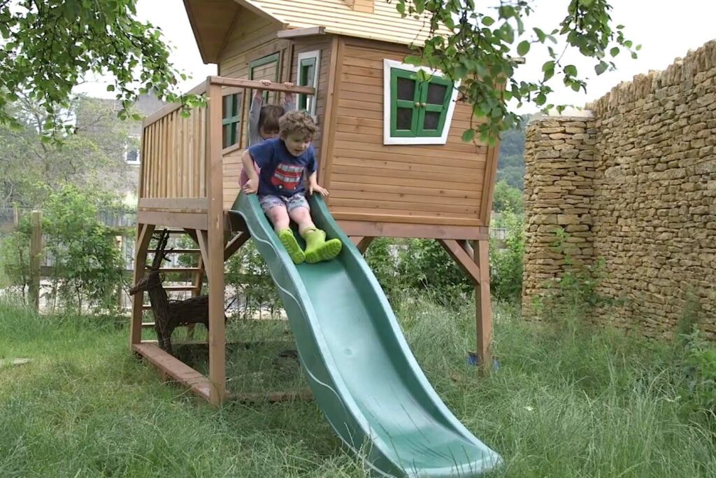 Young child boy Felix going down a green slide in the garden with his sister