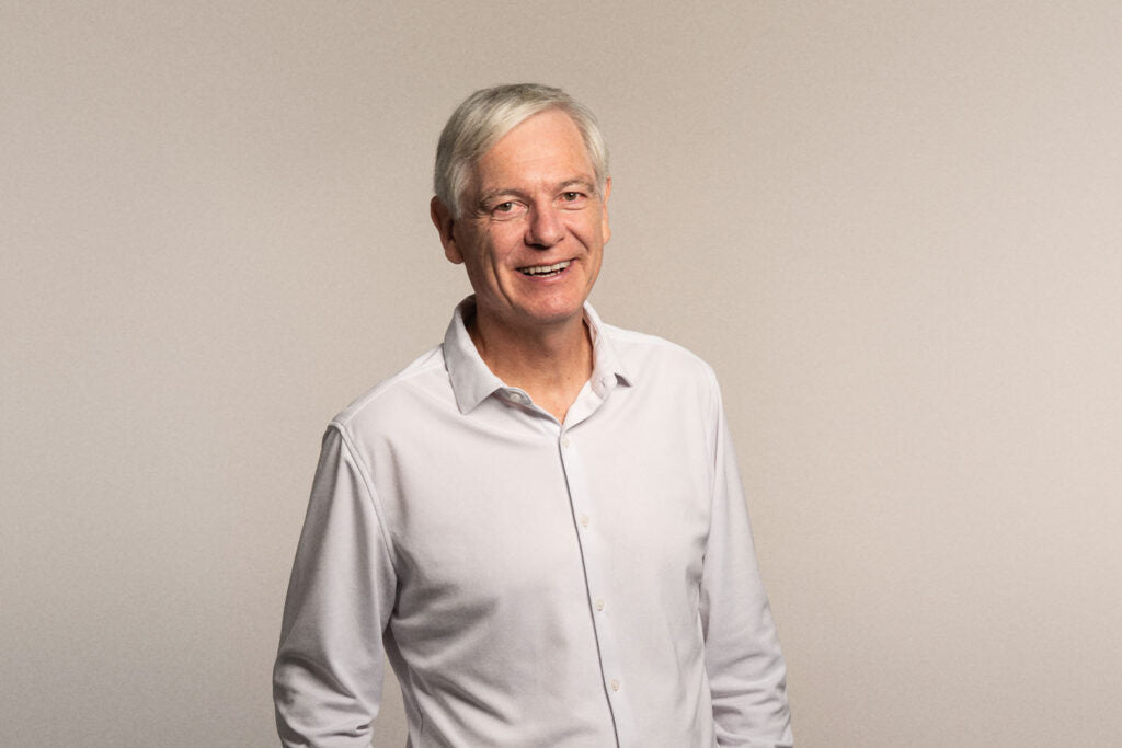 Doctor Wolfgang Brysch in a white shirt, smiling at the camera, with a nude grey background, scientist and founder at iüLabs